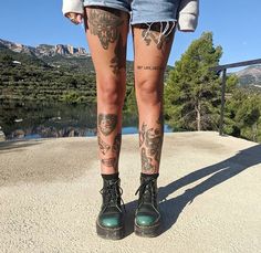 a person with tattoos on their legs and leggings standing in front of a lake