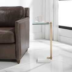 a glass table with a cup on it next to a brown leather chair and window