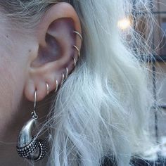 a close up of a person wearing ear rings and piercings on their ears with white hair