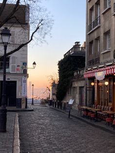 a cobblestone street lined with tables and chairs next to tall buildings at sunset