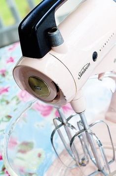 a pink mixer sitting on top of a glass table next to a flower covered tablecloth