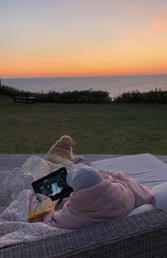 a person laying on top of a bed next to the ocean with a laptop computer