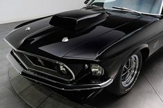 an old black muscle car is parked in a room with white walls and flooring