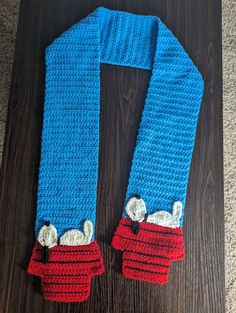 a blue scarf with red and white crochet on it sitting on top of a wooden floor