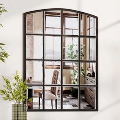 a mirror reflecting a living room and kitchen area with plants in vases next to it