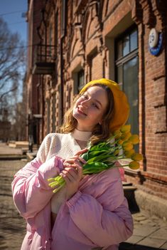 a woman in a yellow hat and pink coat is holding tulips on the street