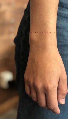 a woman's hand with a small dotted line tattoo on her left wrist,