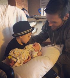 a man holding a baby in a hospital bed next to another person with a hat on