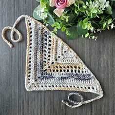 a crocheted triangle is sitting next to some flowers and greenery on a table