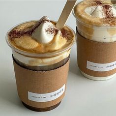 two cups of coffee with whipped cream and chocolate toppings, one has a spoon in it