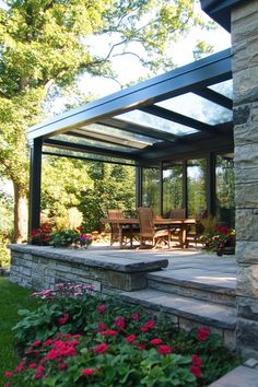 Glass-roofed patio with wooden dining set, surrounded by lush greenery and blooming flowers. Outdoor Topiary, Canvas Awnings, Dining Patio, Retractable Shade, Corrugated Metal Roof