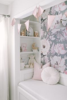 a baby's room with floral wallpaper and pink accessories on the shelves, along with a white crib