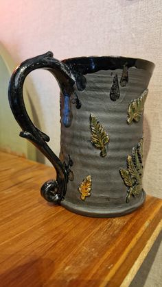 a ceramic mug with leaves on it sitting on a wooden shelf next to a wall