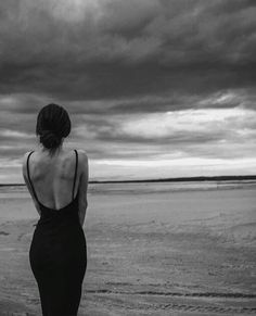 a woman standing on top of a beach next to the ocean under a cloudy sky