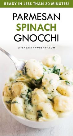 a white bowl filled with pasta and spinach on top of a table next to a spoon