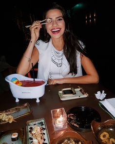 a woman sitting at a table with food in front of her and holding chopsticks up to her mouth