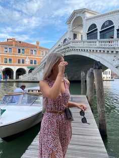 a woman standing on a dock next to a boat in the water and looking up into the sky