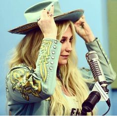 a woman wearing a cowboy hat and holding her head in front of a microphone while standing next to a blue wall