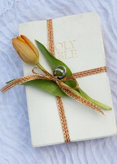 an open book with a ring on it and a tulip in the middle, sitting on a white blanket