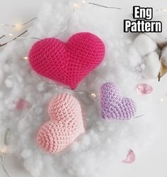 two crocheted hearts sitting on top of white fluffy material next to cotton balls