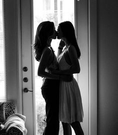 two women kissing each other in front of a door with the light coming through them