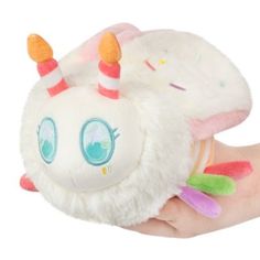 a hand holding a white stuffed animal with colorful horns and eyes on it's face