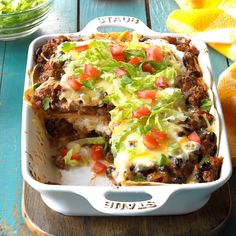 a casserole dish with meat, cheese and lettuce in it on a wooden table