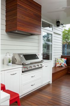 an outdoor kitchen with wood flooring and white cabinets on the side of a house