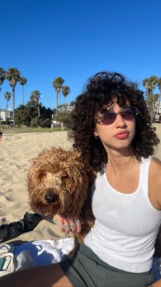 a woman sitting on top of a beach holding a brown dog next to her chest