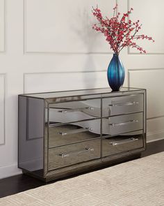 a blue vase with flowers on top of a silver dresser