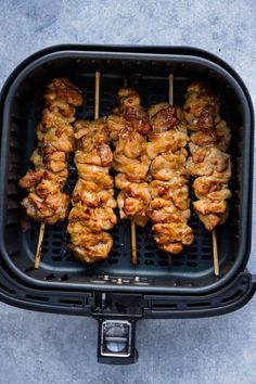 chicken skewers are being cooked in an air fryer on a gray surface