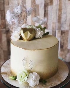 a white cake with gold decoration and flowers