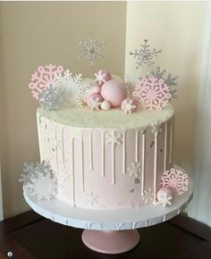 a pink and white cake with snowflakes on it sitting on a wooden table