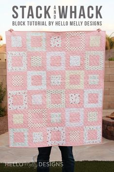 a person holding up a pink and white quilt in front of a brick wall with the words stack and whack written on it