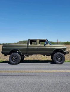 a green truck parked on the side of a road next to a grass covered field