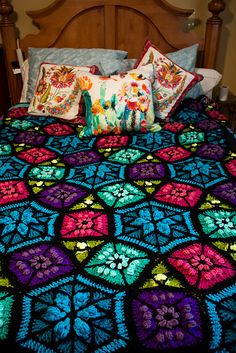 a bed covered in colorful crocheted bedspread and pillows