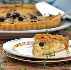 a slice of quiche on a plate next to another pie with olives and herbs