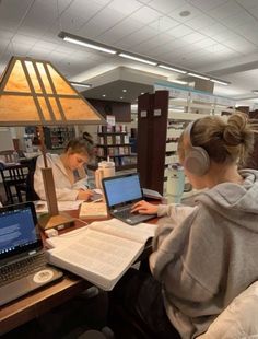 two women sitting at a table with laptops and books