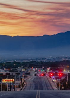 an empty street with mountains in the background at sunset or sunrise, and red traffic lights on both sides