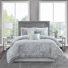 the comforter is made up with grey and white bedding, along with two nightstands