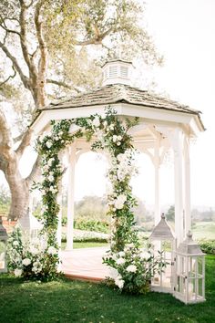 a white gazebo with flowers and greenery around it