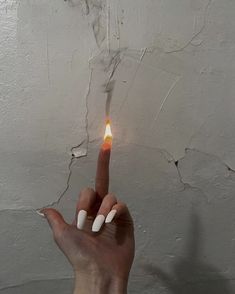 a person's hand holding a lit matchstick in front of a white wall