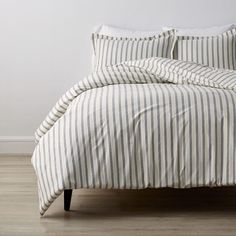 a bed with white and blue striped sheets on top of it, next to a wooden floor