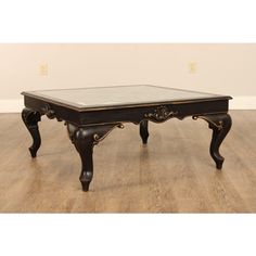 an antique coffee table with glass top and carved legs on wooden flooring in front of a white wall