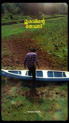 a man standing next to a blue boat on top of a lush green field