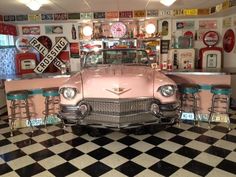 an old pink car is parked in front of two bar stools and a black and white checkered floor