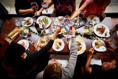 a group of people sitting around a table with food and wine glasses on top of it