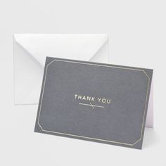 a thank card with the words thank you written on it in gold foil, next to an envelope