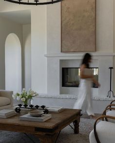 a woman walking through a living room with white furniture and a large painting on the wall