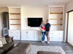 a man and woman standing in front of a flat screen tv mounted on a wall